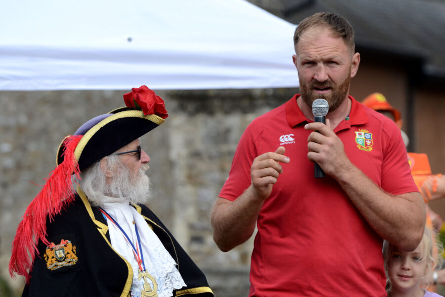 Nathan Hannay speaking at the opening ceremony for Honiton Market Charter Day 2025 outside St Paul's Church, while retiring town crier Dave Retter looks on.